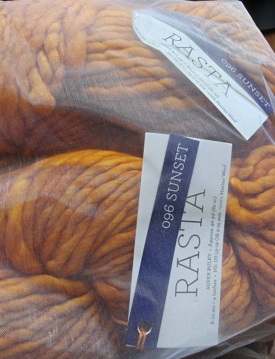 Two skeins of a variegated orange yarn inside of a sheer bag.