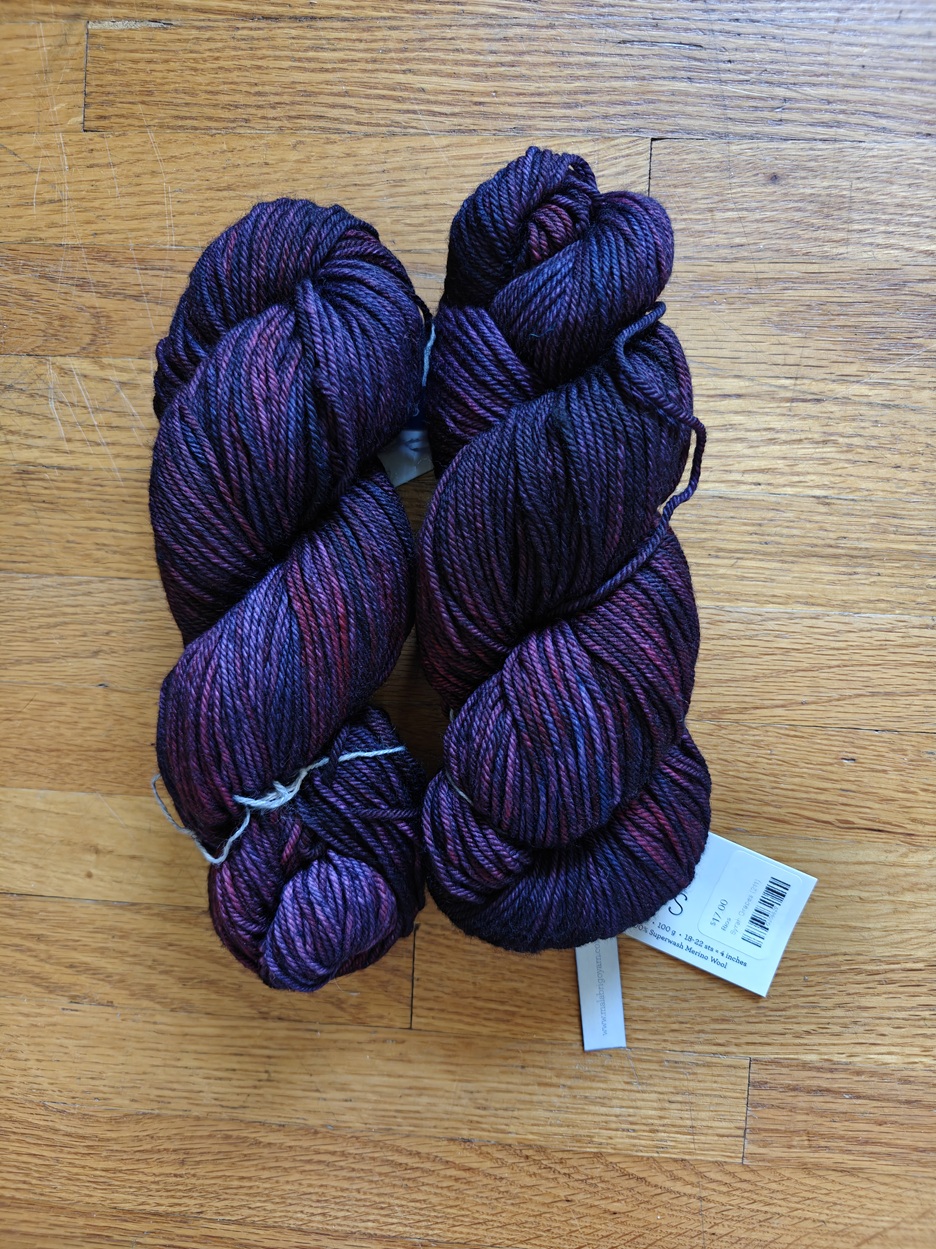 Two skeins of a variegated yarn in dark purple shades on a wooden background.